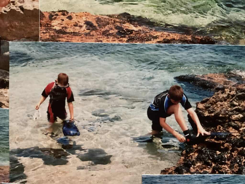 Kindern beim Muschelsammeln am Strand mit Wasser und Felsen.