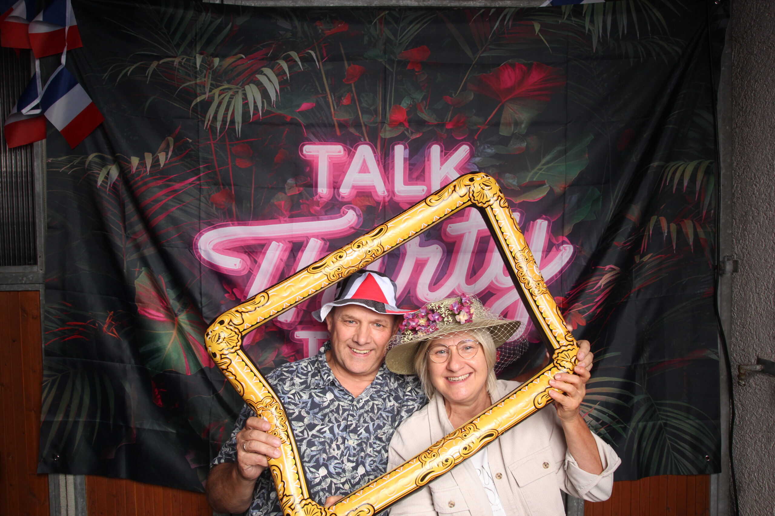 Fröhliches älteres Paar bei 30. Geburtstag mit Blumenhut und Partyhütchen, schöne Feier-Szene, festliche Stimmung, Jubiläum, Geburtstag, Feier, Spaß.