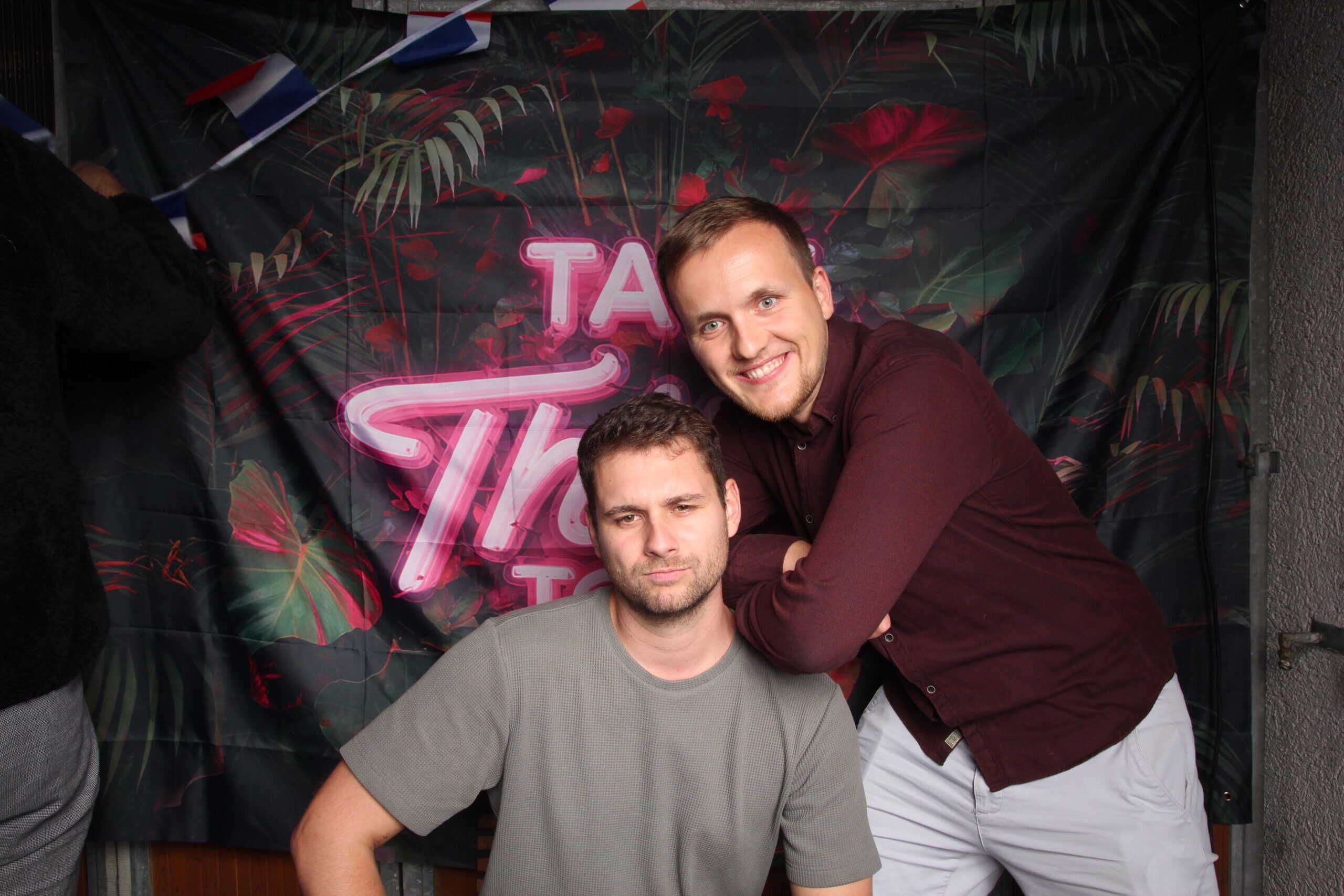 Junges Männer feiern Geburtstag bei einer Party in einer Bar, lachend und posierend vor einem neonbeleuchteten Hintergrund.