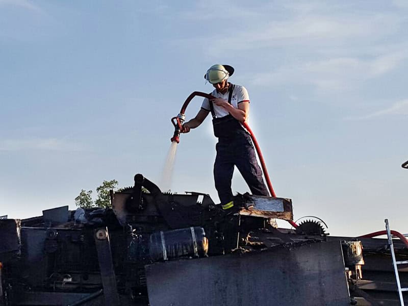 Feuerwehrmann bei der Brandbekämpfung auf demoliertem Fahrzeug, Einsatz bei Feuerlöscharbeiten.