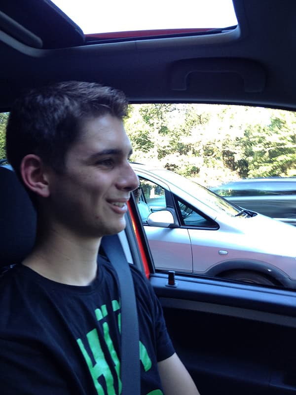 Junger Mann sitzt im Auto, Sonnenbrille, fröhlich, junge Person, Sommerfahrten, Straße, Freundschaft, gefahren, Fahrspaß, Freizeit, Lifestyle, modernes Fahrzeug.