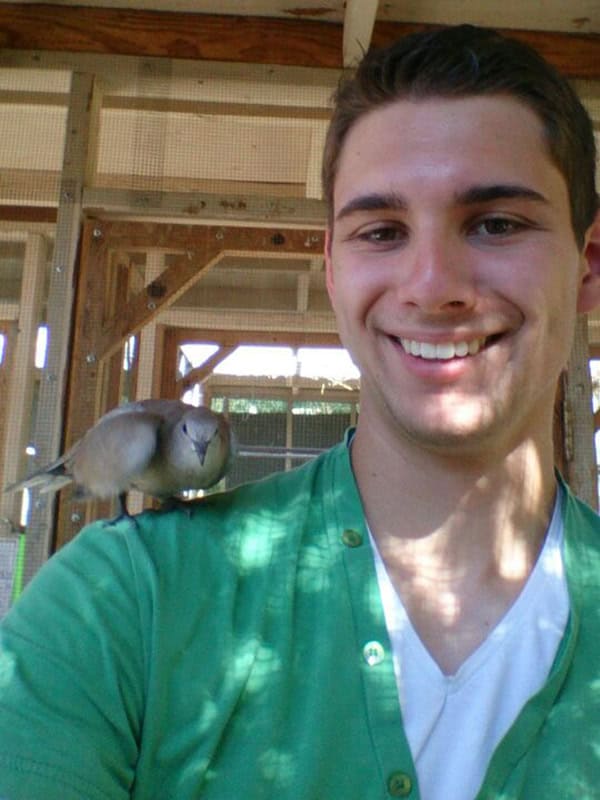 Freudiger junger mann mit vogel auf der schulter in einer holz-veranda.