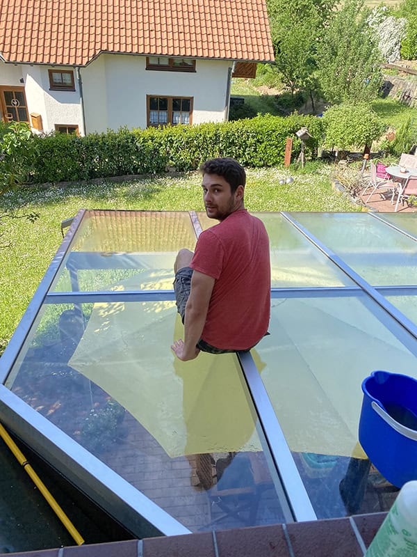 Sonnengefluteter Mann auf Glasdach in Garten, Geburtstag feiern, Relaxen, Outdoor-Atmosphäre, Frühlingswetter.