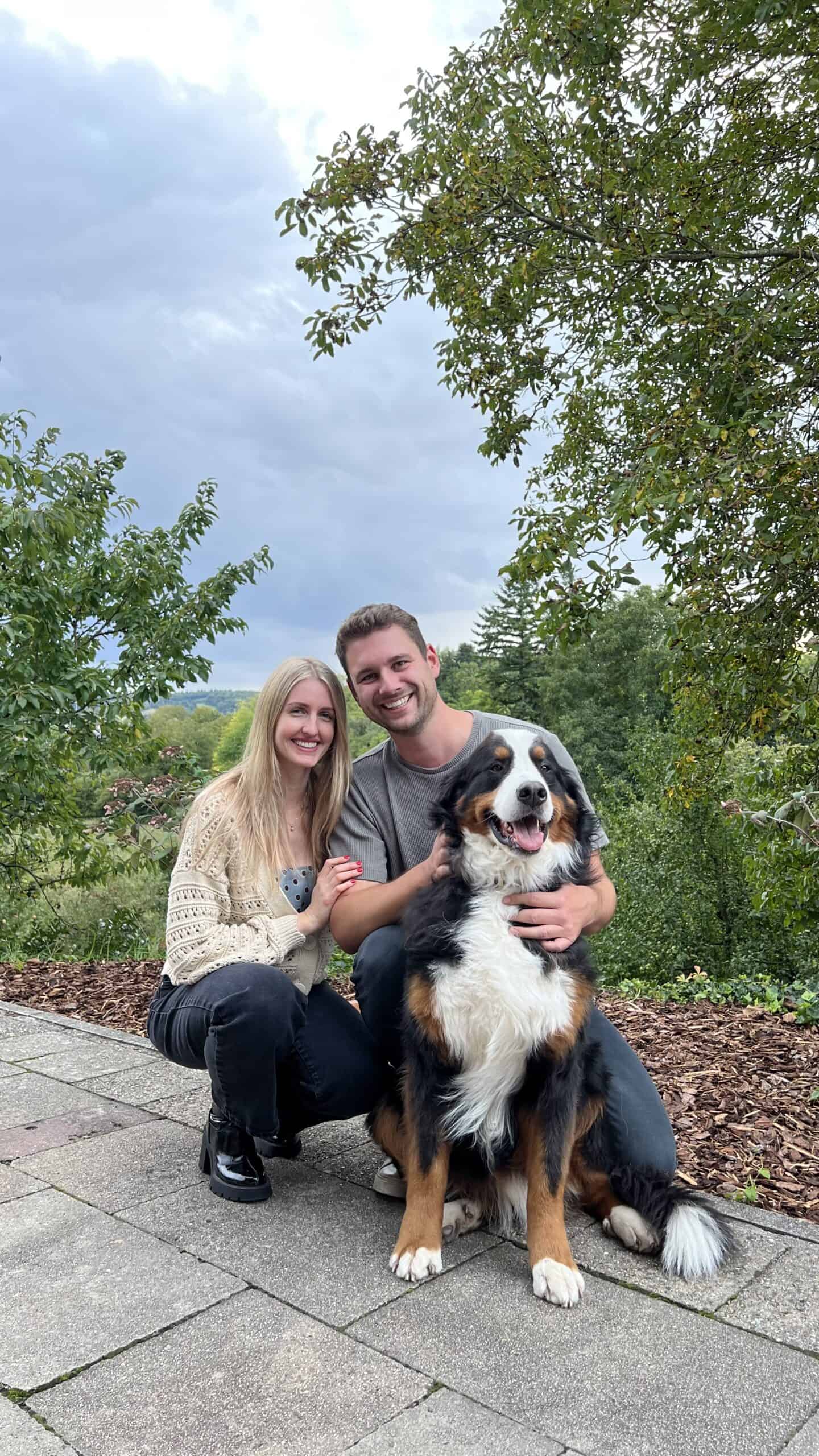 Lächelndes Paar mit Hund im Grünen, zum Geburtstag, Freude und Zusammengehörigkeit, Naturerlebnis, glückliche Momentaufnahme, Hundeliebe, Jubiläumsfeier.