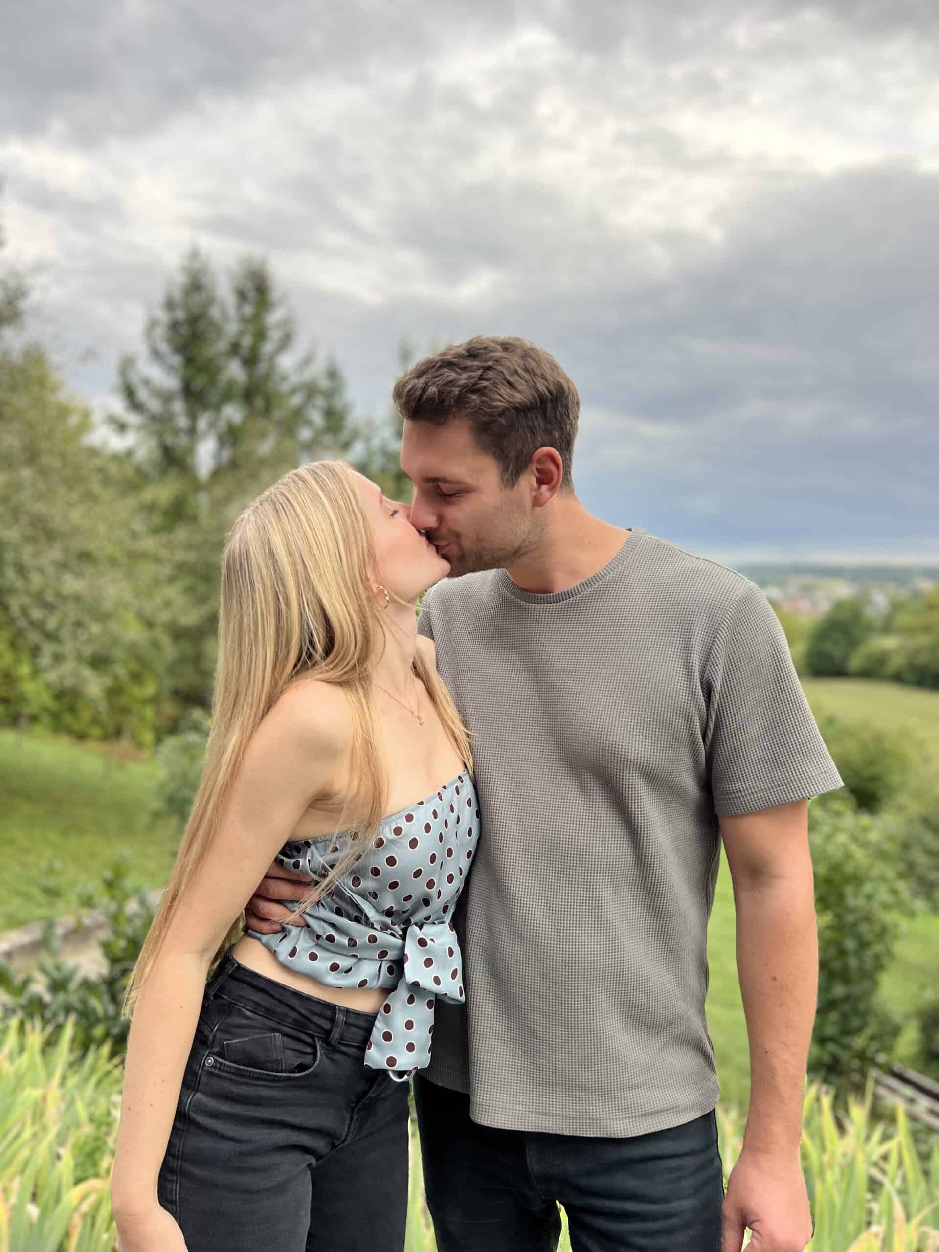 Freundespaar küsst sich im Grünen zu einem Geburtstagsfoto.